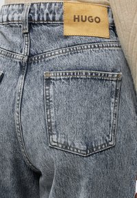 Πίσω όψη γκρι τζιν acid-wash με την δεξιά πίσω τσέπη και ένα ταμπελάκι από ταμπά δέρμα με το λογότυπο HUGO στη μέση.