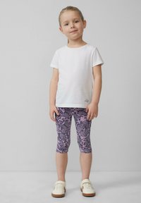 Witte katoenen t-shirt gecombineerd met paarse leggings met een patronen van bladeren en luipaarden. De outfit wordt compleet gemaakt met beige schoenen.
