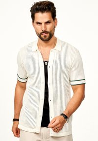 Hemd mit kurzen Ärmeln, Knopfverschluss in Creme mit durchbrochenem Muster und grün gestreiften Manschetten. Leichter Strickstoff für Atmungsaktivität.