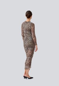 Robe à imprimé léopard à manches longues, présentant un tissu transparent, une silhouette cintrée et un ourlet volants. Portée avec des mules noires à talons ; vue de dos.