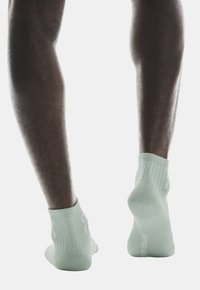 Calcetines tobilleros verde claro con puños acanalados; textura de punto suave, con un diseño de logo sutil en el lateral y un talón reforzado.