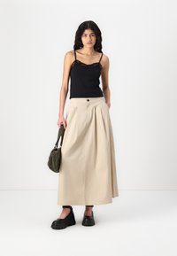 Svart camiskjorte med blondedetaljer i kantene, kombinert med en beige, lang, plisserte skjørt. Svart plattformsko og en olivengrønn skulderveske fullfører antrekket.
