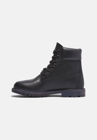 Bottine montante noire en cuir à lacets avec col rembourré et semelle robuste, vue de profil sur un fond uni.