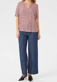 Czerwona i biała, wzorzysta bluzka z krótkim rękawem i dekoltem w szpic, zestawiona z szerokimi, niebieskimi dżinsami i czarnymi butami na slip-on.