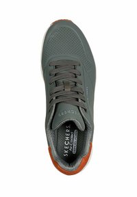 Zapatilla verde con parte superior perforada, cordones grises, acento marrón cerca del talón y plantilla de espuma con memoria. El texto en la plantilla dice "Espuma con memoria refrigerada por aire."