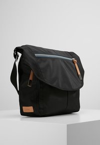 Borsa a tracolla nera realizzata in tessuto resistente, dotata di chiusura a pattina, scomparto frontale con zip e dettagli in pelle marrone chiaro.