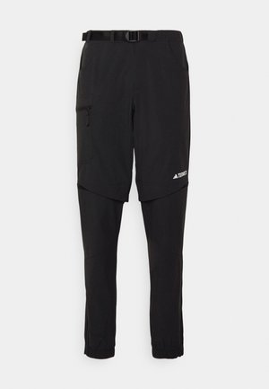 Black outdoor pants with a belt, featuring a zippered side pocket, tapered leg design, and elastic cuffs at the ankles. Brand logo is visible.