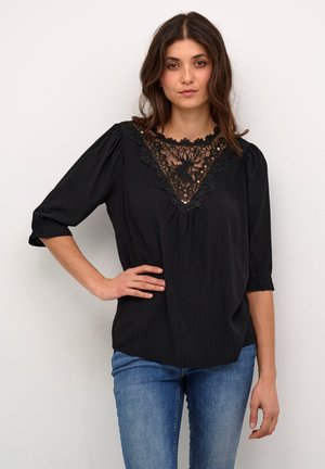 Black blouse with a V-shaped lace neckline, short puff sleeves, and vertical pinstripe pattern. Paired with blue denim jeans.