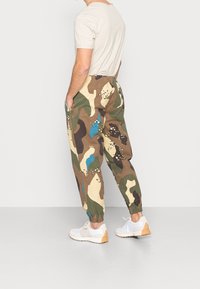 Camouflage joggers in groen, bruin en crème met blauwe accenten, voorzien van een elastische tailleband, zijzakken en bijgebogen enkels.