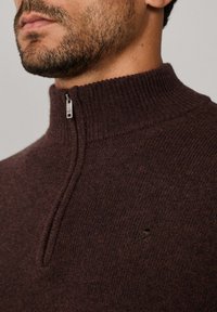 Maglione marrone con zip al collo, realizzato in tessuto a maglia testurizzato. Presenta un colletto a coste alto e un piccolo logo vicino alla spalla.