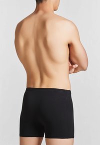 I boxer in cotone neri presentano una vestibilità aderente e una texture liscia, con un design semplice e senza marchi o motivi visibili.