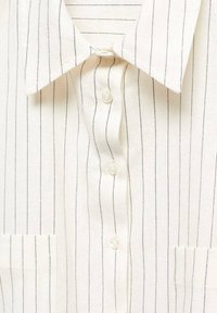 Chemise blanche boutonnée avec de fines rayures verticales noires, un col pointu et une texture de tissu visible.