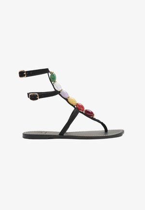 Flad sort sandal med ankelremme og flerfarvede ovale perler langs T-remmen på hvid baggrund.