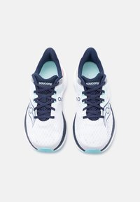 Άσπρα και ναυτικά παπούτσια για τρέξιμο Saucony με πετρόλ εσωτερικά πέλματα, διχτυωτά πάνω μέρη και μαύρα κορδόνια, τοποθετημένα δίπλα το ένα στο άλλο σε ανοιχτό φόντο.