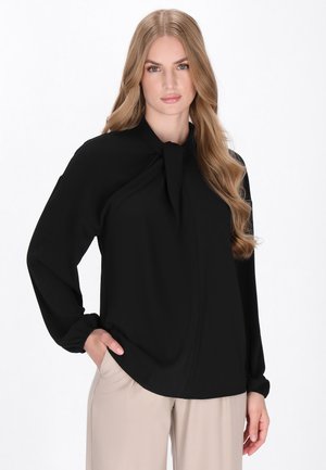 Blouse noire avec un détail de nœud à col, manches longues et un tissu doux et lisse. Le design présente une coupe décontractée et drapée.