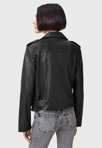 Svart skinnjakke med en tettsittende design, skulderepaulettes og en lett kortet lengde. Kombinert med grå denimbukser.