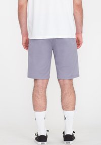 Graue Shorts aus einem weichen Stoff, in mittellanger Länge bis zum Oberschenkel, mit einem schlichten Design. Tragen Sie sie mit weißen Sportsocken und schwarzen Schuhen.