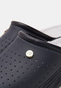 Tengeri bőr slip-on cipők perforált mintával, arany színű kiegészítőkkel és kontrasztos varrással. Puha tapintású, lekerekített forma.
