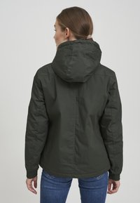 Mørk grønn hettejakke med elastiske ermer og en glatt tekstur. Har et uformelt design som passer for utendørsbruk.
