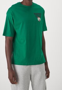 Grön bomull t-shirt med korta ärmar, med texten "BOSTON CELTICS" och en grafisk logotyp på bröstet. Slät textur och ledig passform.