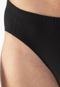 Culotte en coton noir avec une ceinture douce et élastique et des coutures plates, offrant un ajustement lisse et une couverture minimale. La texture semble douce.