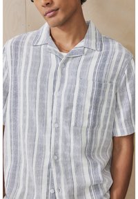Koszula na guziki z krótkim rękawem w biało-granatowy paskowany wzór, z kołnierzykiem, pojedynczą kieszenią na piersi oraz lekką lnianą fakturą.