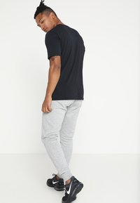 Camiseta negra de cuello redondo, combinada con pantalones de chándal gris claro. El calzado presenta un diseño negro con acentos blancos. Look simple y casual.
