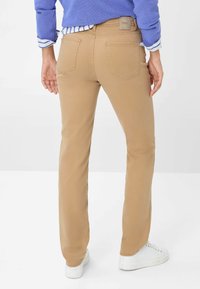 Jeans beige clair avec une coupe droite, dotés de poches arrière et d'une étiquette en cuir avec logo. Associés à des baskets blanches.