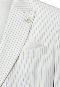 Blazer mit weißen und blauen Streifen, der eine Gänseblümchen-Nadel und ein gemustertes Einstecktuch trägt. Textil mit Struktur und taillierter Form.