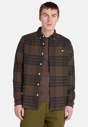 Bruin geruit overhemd met donkere marine lijnen, voorzien van een button-down kraag, borstzak en plastic knopen, gedragen over een bruin t-shirt.