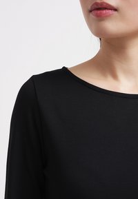 Czarna bluzka z długim rękawem i okrągłym dekoltem, wykonana z gładkiego, elastycznego materiału. Brak widocznych wzorów lub akcentów.
