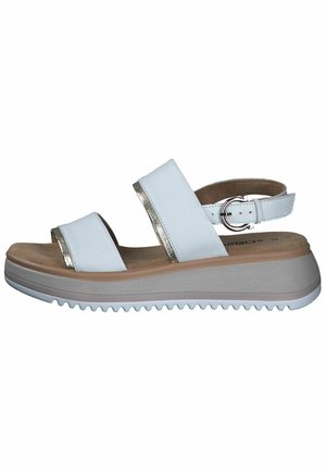 Weiße Sandalen mit zwei breiten Riemen, die metallische Akzente aufweisen, einem gepolsterten Fußbett und einer geriffelten, hellen Keilsohle. Mit Schnallenverschluss an der Ferse.