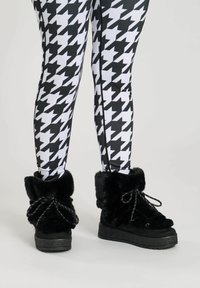 Black fur ankle boots with textured upper, plush accents, and black laces. Paired with white and black houndstooth patterned leggings.