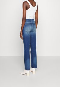 Jeans de denim con corte recto, lavado azul medio y un ligero desvanecimiento. Presenta dos bolsillos traseros y se lleva con botines blancos de tacón.