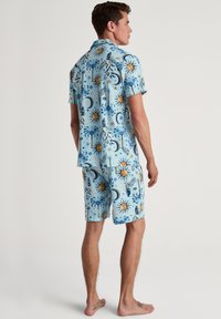 Korte mouwen lichtblauw shirt en shorts set met gele zonnen, palmbomen en abstracte ontwerpen, gemaakt van een gladde, lichte stof.