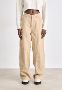 Beige wide-leg pants made of cotton, featuring front pockets and a high waist, paired with white cropped sweater and chunky white boots.