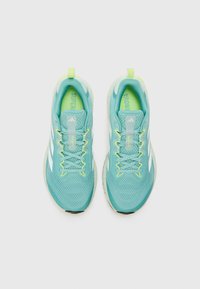 Zapatillas deportivas turquesas con parte superior de malla, que reflejan la luz, con acentos amarillos en los cordones y el logo, y lengüeta acolchada, diseñadas para mayor comodidad y soporte.