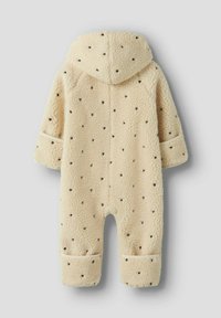 Combinaison en polaire beige avec capuche, dotée d'une texture douce, de motifs en forme de cœur foncés et de manches à poignets.