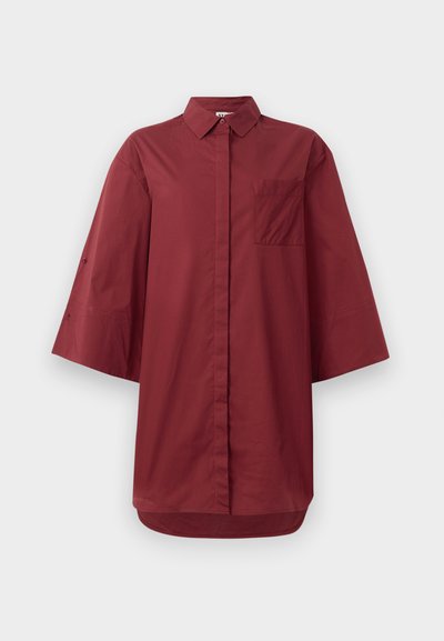 Camisa oversized bordô com colarinho abotoado, mangas curtas e largas, um bolso no peito e uma bainha curvada. Feita de um tecido de algodão suave.