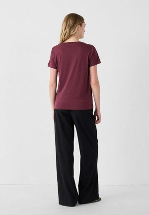 Camiseta burdeos de manga corta con cuello redondo, combinada con pantalones negros holgados, vista desde la parte trasera contra un fondo liso.