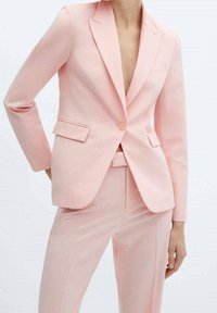 Blazer rose pâle ajusté avec revers crantés, fermeture à un bouton, deux poches avant et coupe slim. Tissu à texture lisse et design sur mesure.