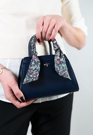 Petit sac à main en cuir bleu marine avec une écharpe florale en tissu nouée sur les poignées, détails en métal doré, forme structurée et texture lisse.
