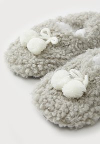 Comodi pantofole grigie lavorate a maglia con texture morbida, caratterizzate da due pompon bianchi e un accento con nodo a loop. Interno morbido e peloso.