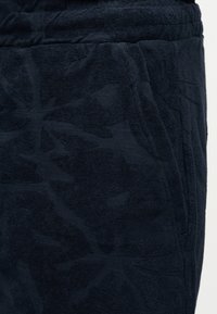 Κοντινό πλάνο μαύρων βερμούδων από πετσέτα με υφή λουλουδιών και πλαϊνή τσέπη με ελαστική μέση.