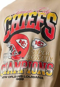 Kansas City Chiefs -logo ja kypärä, jossa teksti "Super Bowl IV -mestarit New Orleans Louisiana 1969" vaalealla kankaalla.