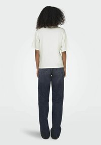 Lichtbeige T-shirt met korte mouwen en een boxy pasvorm, gecombineerd met donkerblauwe straight-leg jeans. Zachte katoentextuur, geen zichtbare patronen.