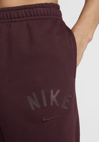 Bordeaux Nike sweatpants med elastisk midjeband, med en tonal logotryck och en liten broderad detalj. Slät tygtextur.
