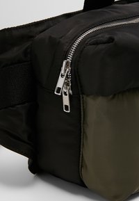 Borsa in tessuto nera e verde oliva con forma rettangolare, dotata di chiusura a zip doppia in argento e superficie testurizzata.