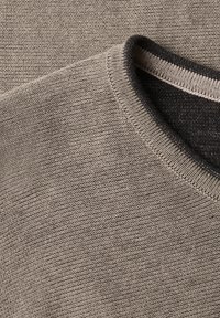 Gros plan d'un pull en maille beige avec un col rond présentant une doublure intérieure gris foncé et des bords finement côtelés.