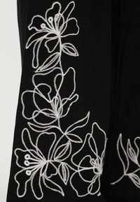 Μαύρο ύφασμα με λευκό κεντητό μοτίβο φυλλωτού κλήματος με μεγάλα ανοιχτά λουλούδια και φύλλα.